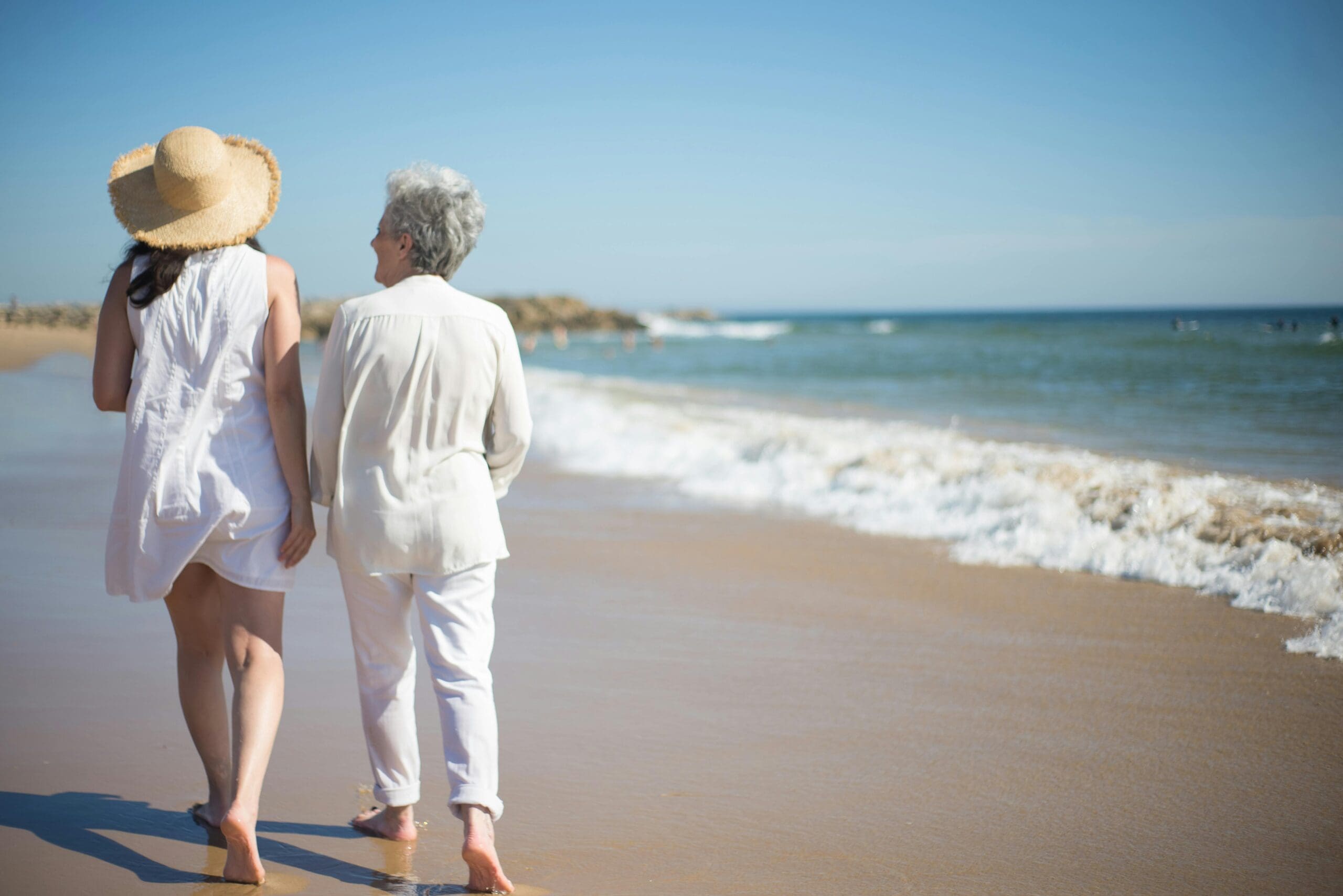 Two women walking barefoot on the beach, symbolizing grounding, connection, and energetic restoration in an overstimulated world.